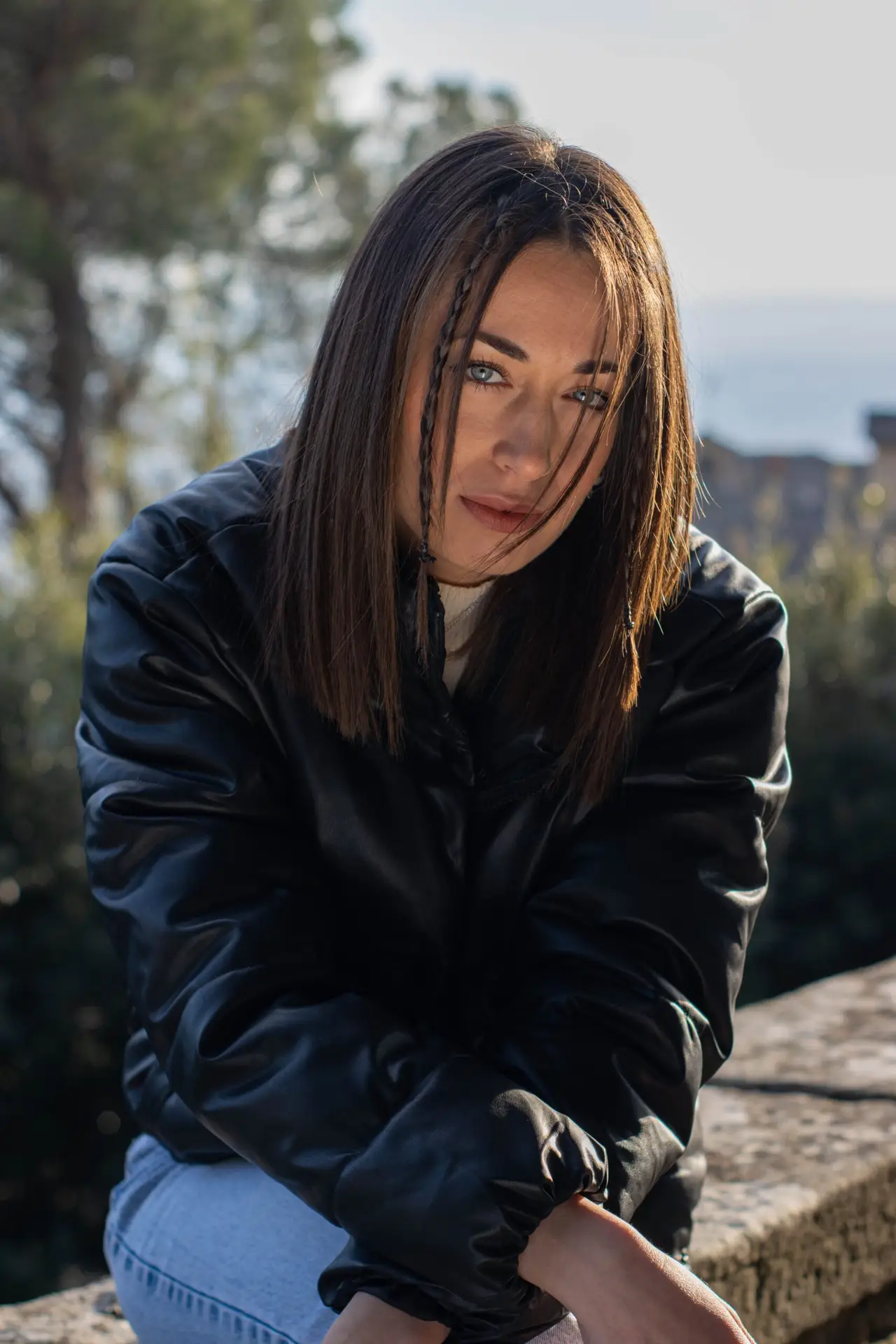 Fashionable brunette woman in a leather jacket, posing outdoors with a pensive look.