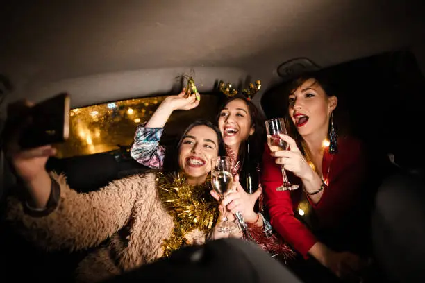 three modern young women celebrating new year's eve at the back seat of a car